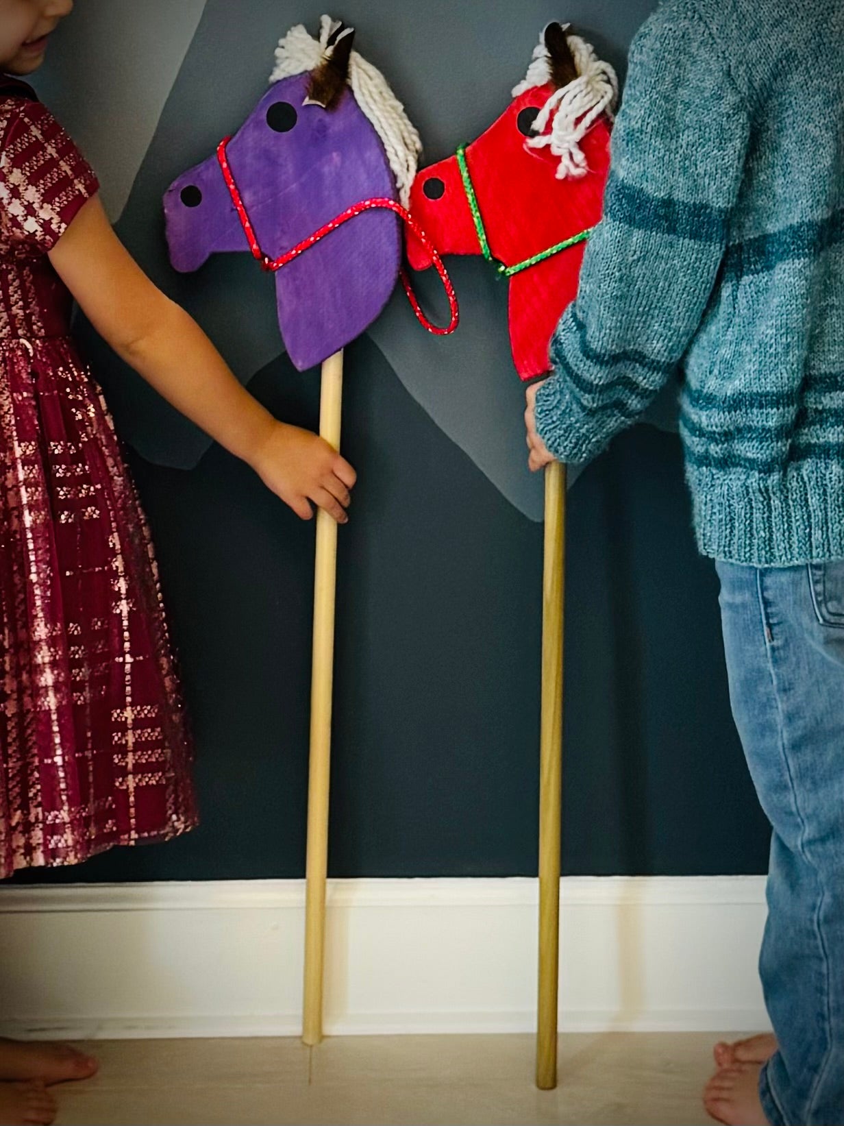 Children holding colorful kids wooden hobby horses with yarn manes and decorative reins indoors