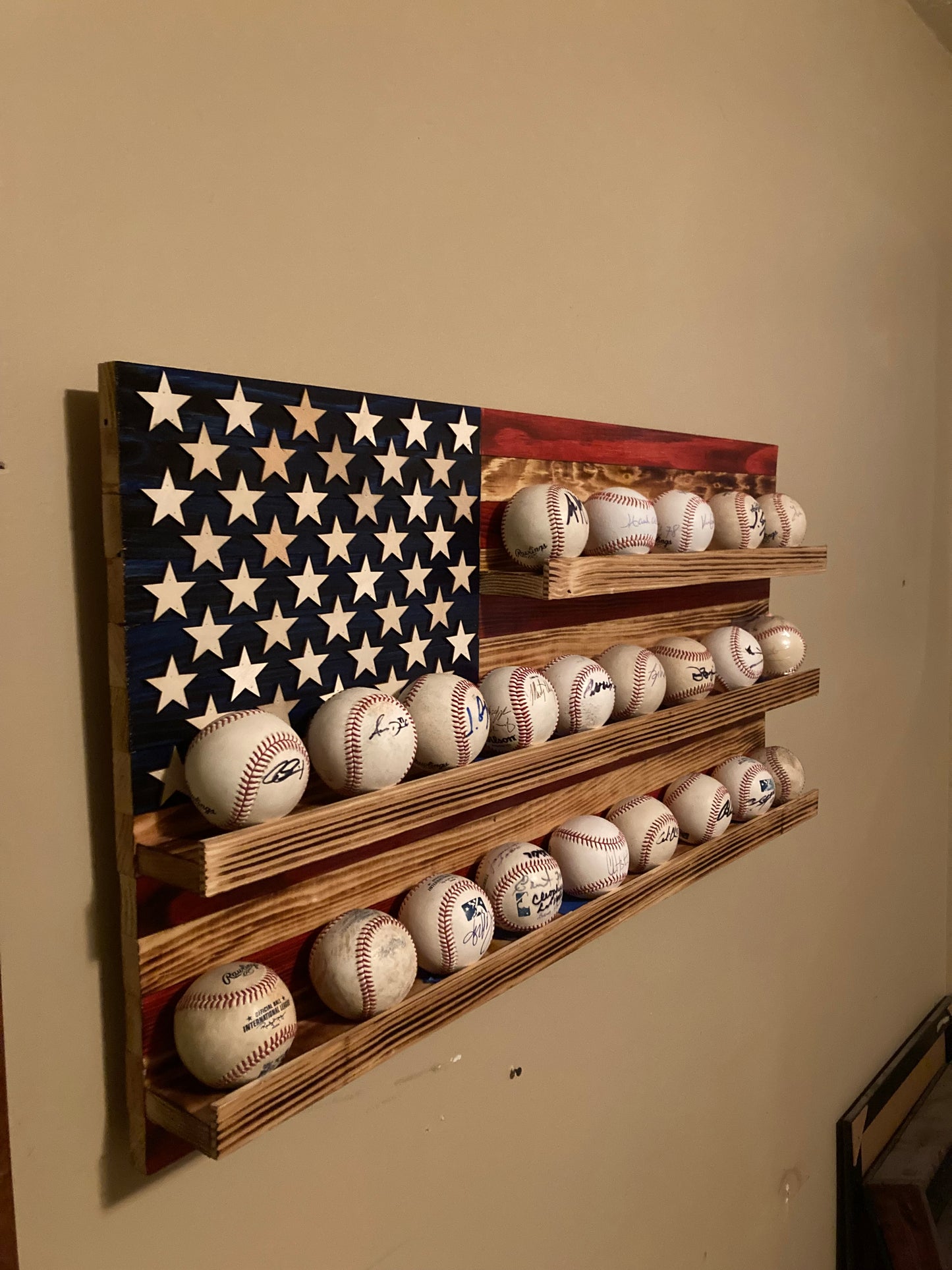 American flag baseball rack display mounted on wall holding multiple signed baseballs
