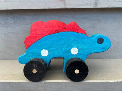 Handcrafted dinosaur kids pull toy in blue and red with black wheels on wooden surface