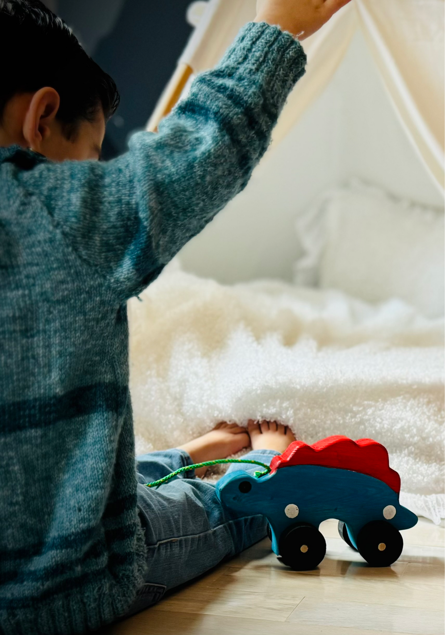 Child playing with handcrafted dinosaur kids pull toy in blue and red on wooden floor