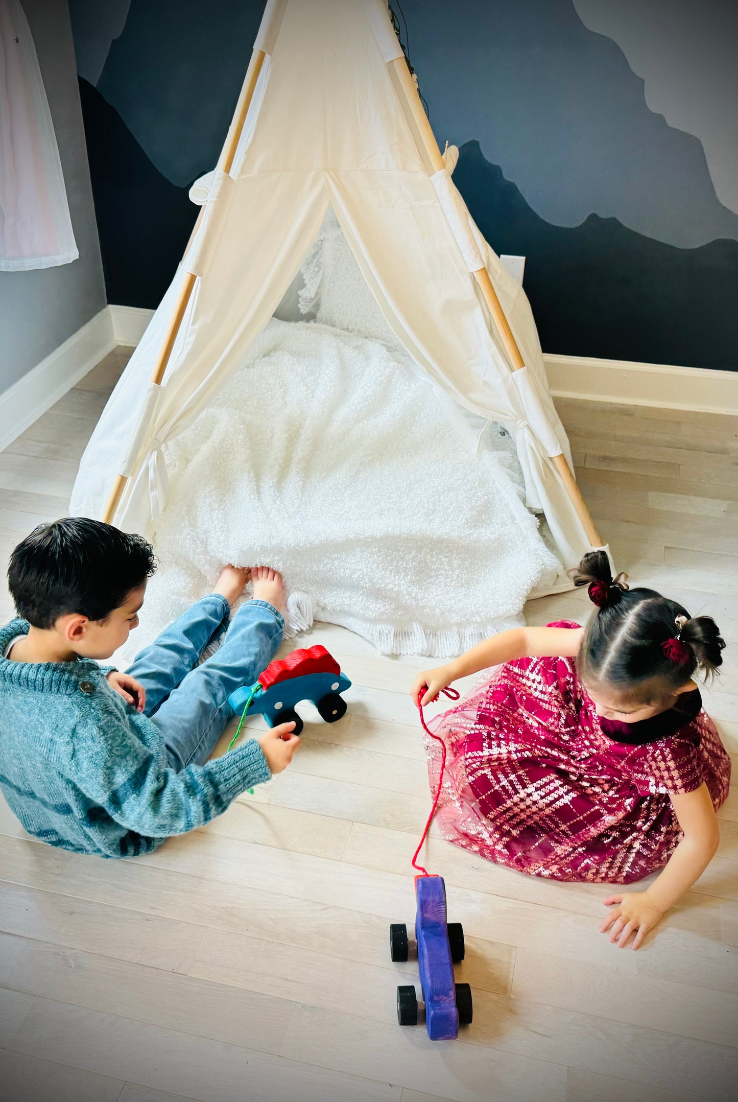 Two children playing with handcrafted dinosaur kids pull toy by a white play teepee on wooden floor