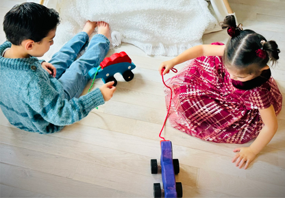 Two kids playing with a handcrafted dinosaur kids pull toy on a wooden floor near a white rug