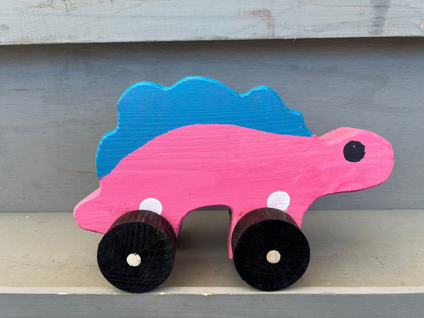 Handcrafted dinosaur kids pull toy painted pink and blue with black wheels for children