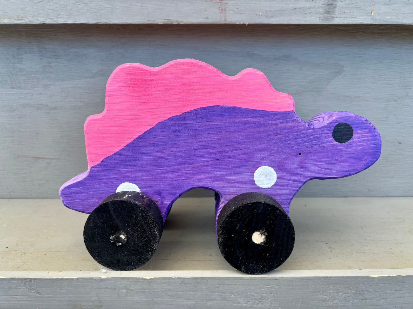 Handcrafted dinosaur kids pull toy in purple and pink wood with black wheels