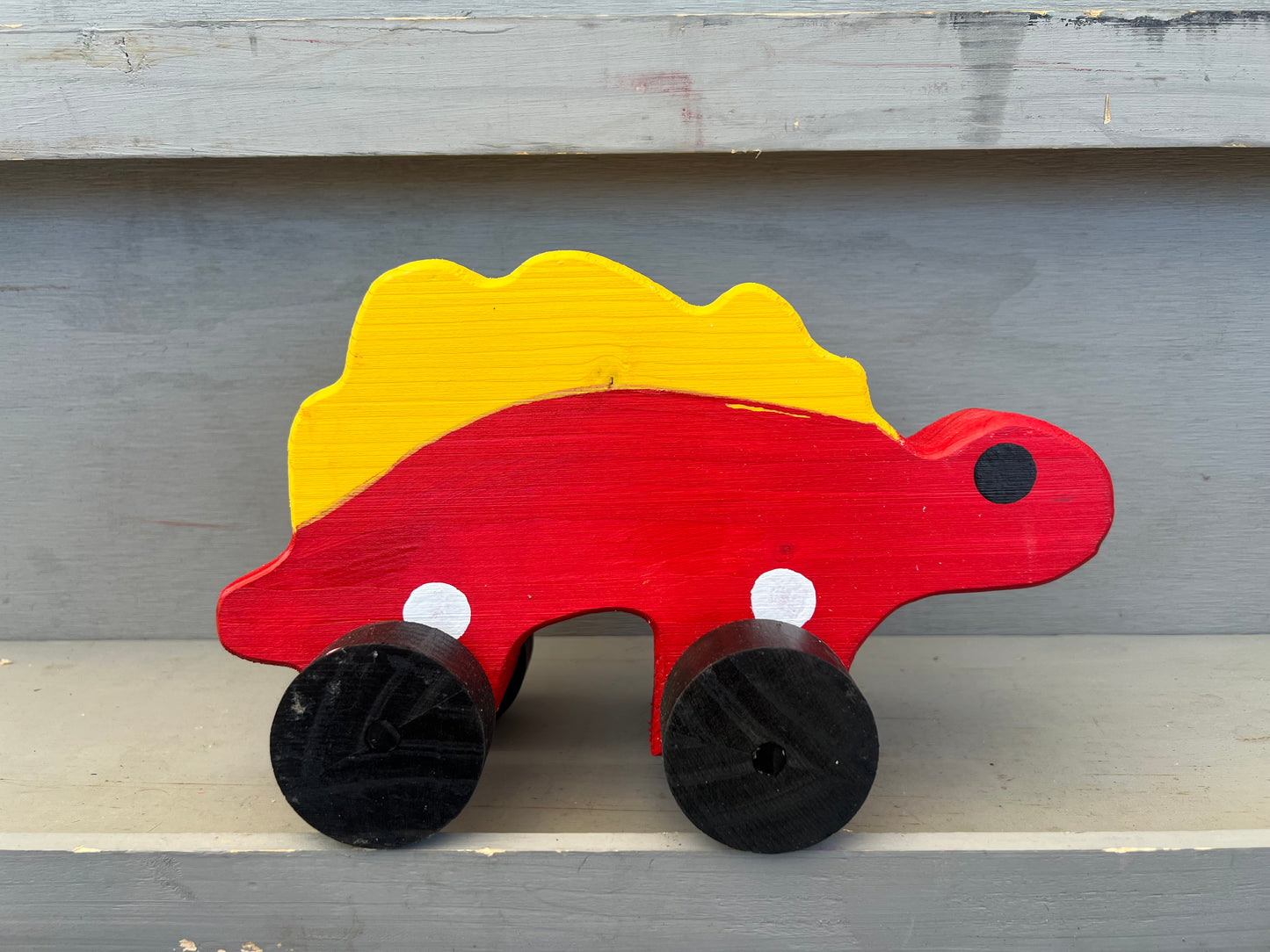 Handcrafted dinosaur kids pull toy in red and yellow with black wheels on a wooden surface