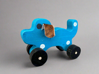 Blue handmade wooden dog pull kids toy with black wheels and brown ear on gray background