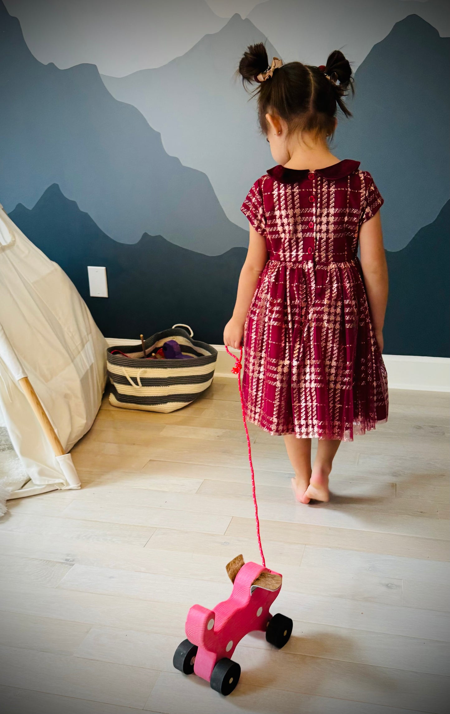 Child playing with handmade wooden dog pull kids toy in pink with black wheels indoors