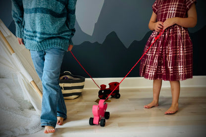 Children playing with a handmade wooden dog pull kids toy on a hardwood floor indoors