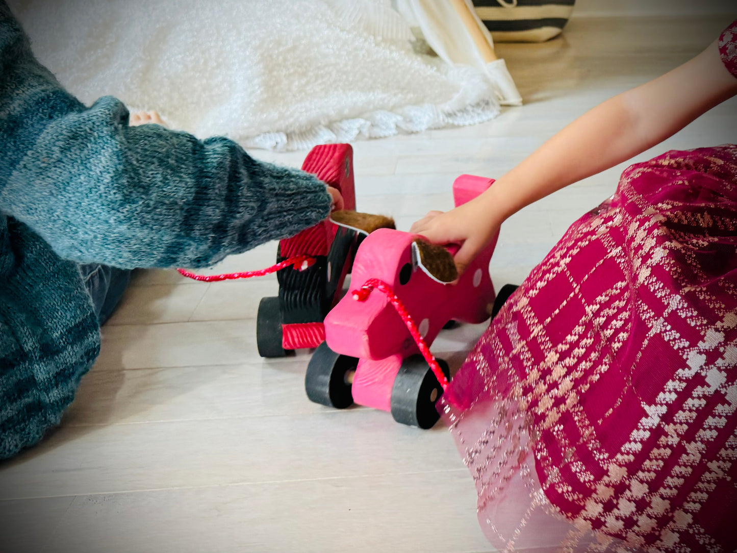 Children playing with a handmade wooden dog pull kids toy in bright pink color on wooden floor