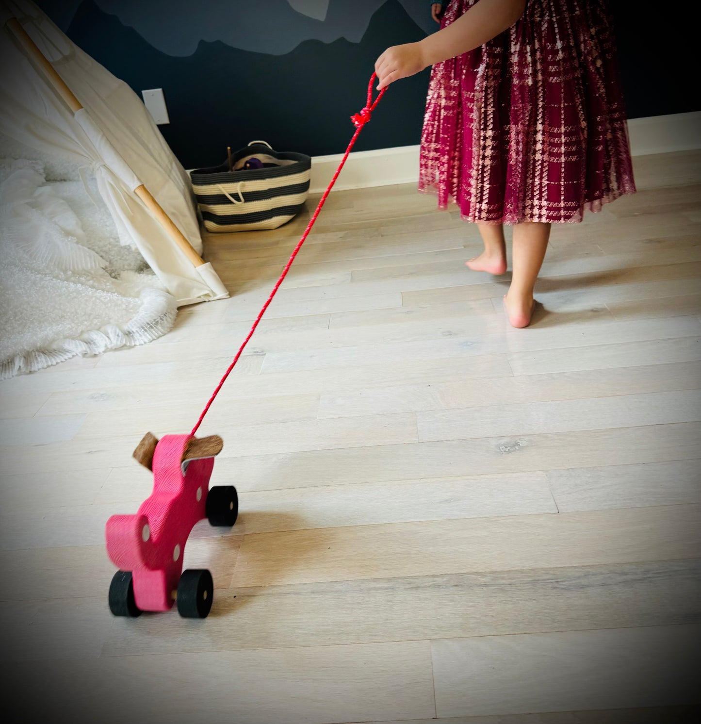 Child playing with a handmade wooden dog pull kids toy with red string on wooden floor