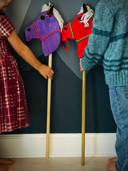 Children holding colorful kids wooden hobby horses with yarn manes and decorative reins indoors