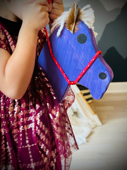 Child holding a blue kids wooden hobby horses with red reins and white mane indoors