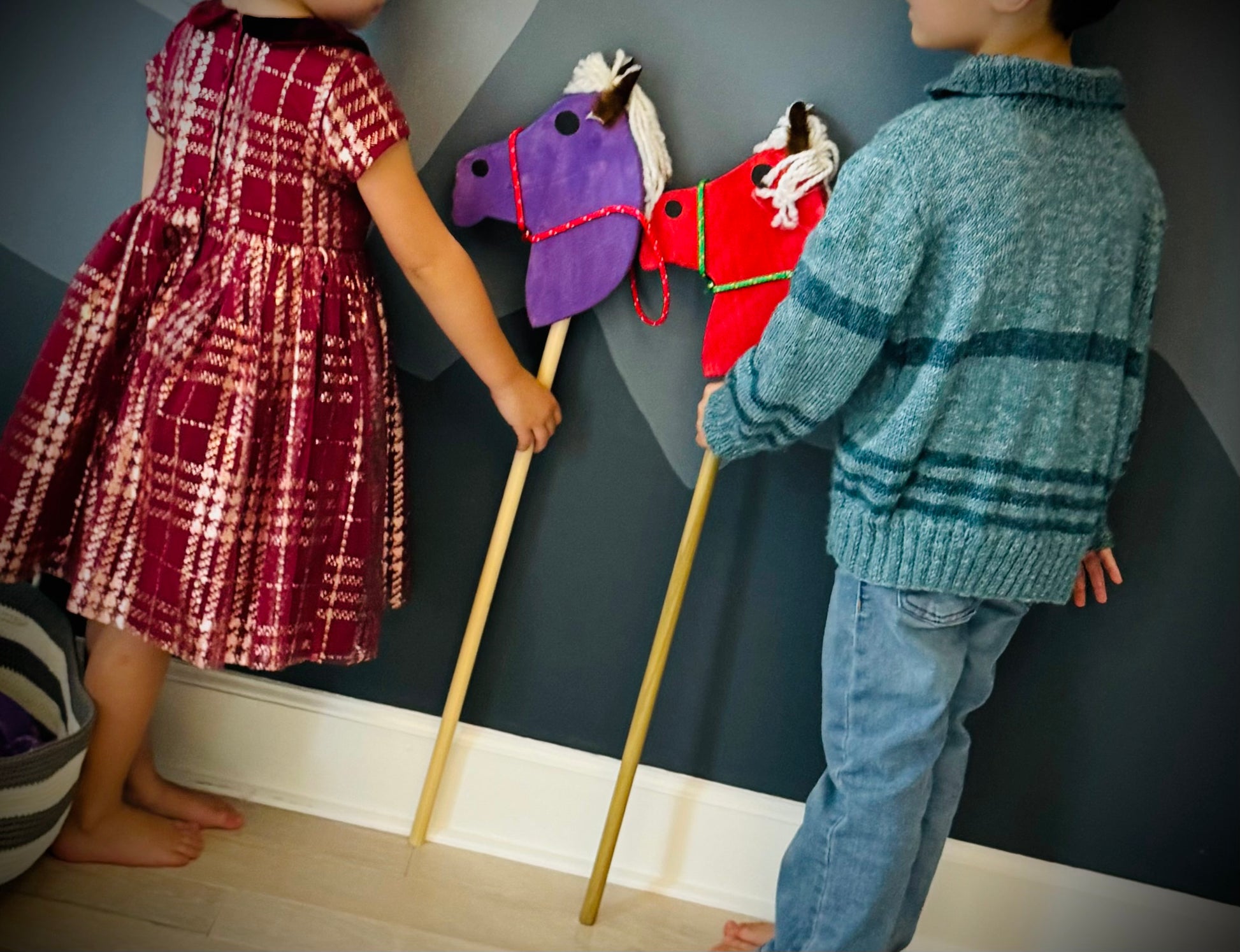 Two children playing indoors with colorful kids wooden hobby horses with fabric horse heads on wooden sticks