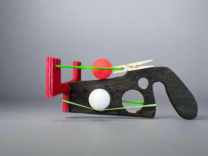 Kids wooden ping pong ball launcher in black and red with green rubber bands and ping pong balls