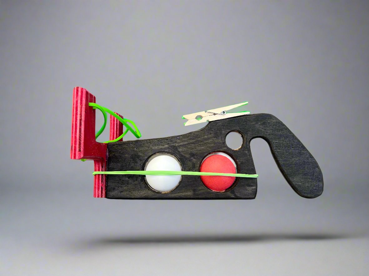 Kids wooden ping pong ball launcher with red and black design holding two ping pong balls