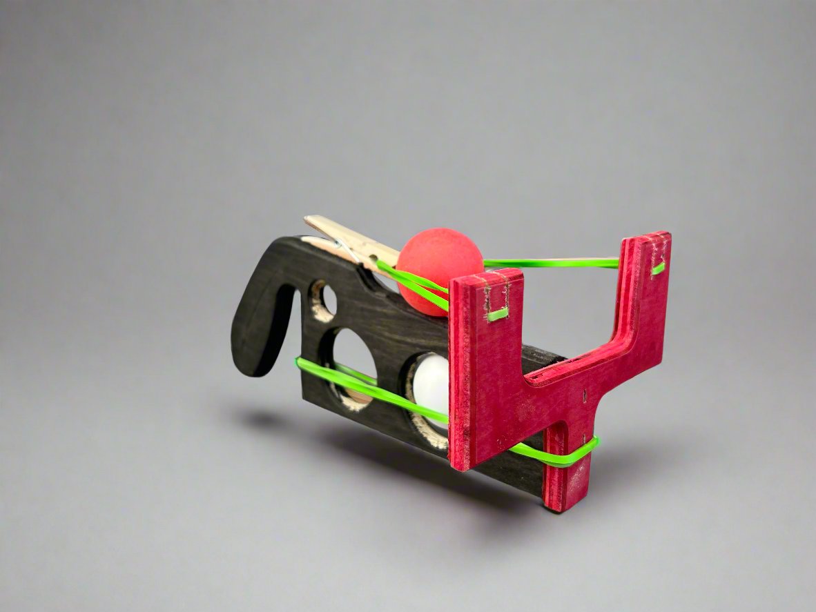 Kids wooden ping pong ball launcher with red and black wooden frame and green rubber bands