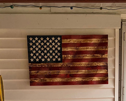 Rustic American flag wall art made of wood with natural grain and distressed paint hanging on white siding