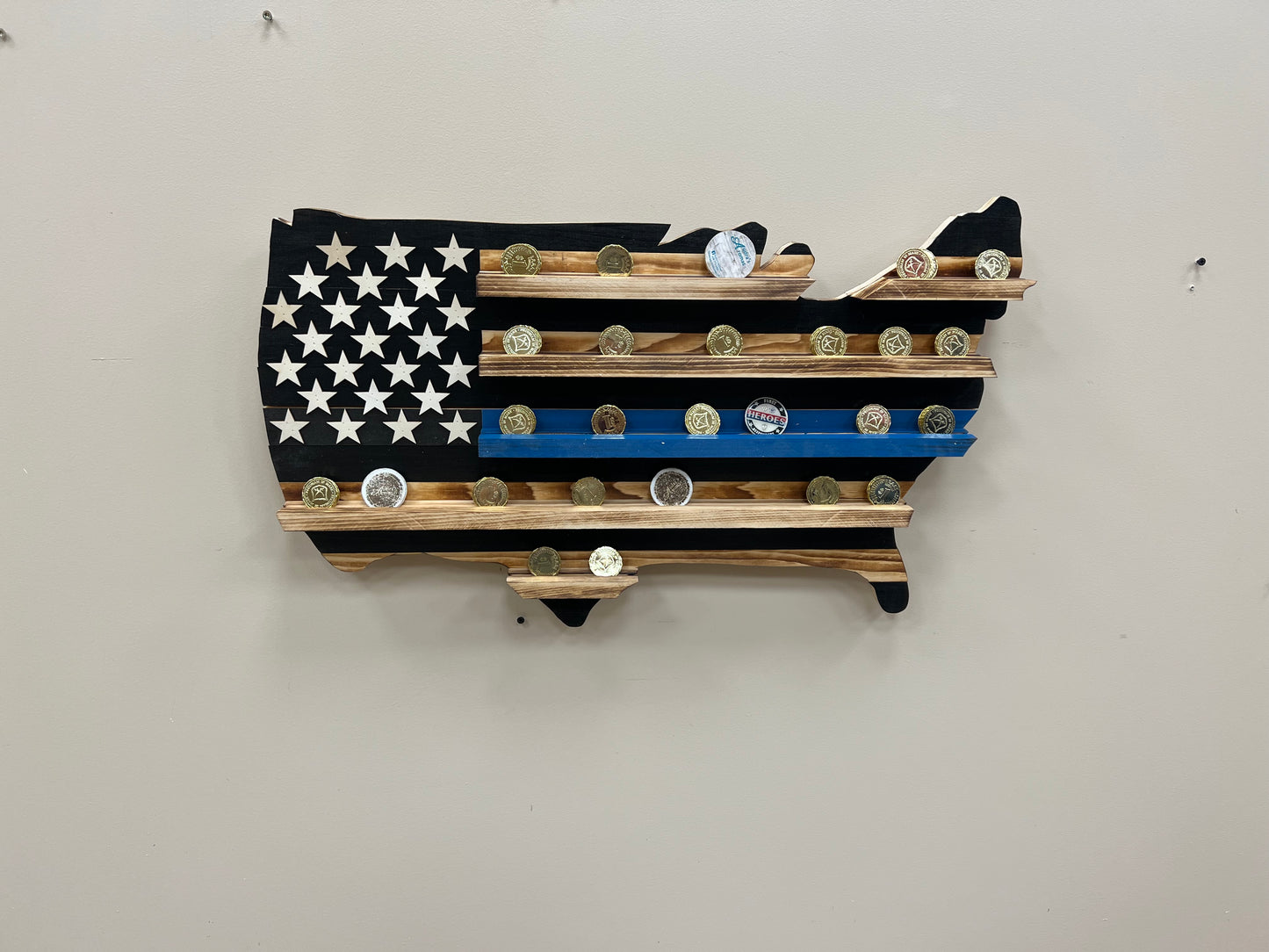 Thin blue line challenge coin holder wall art shaped like the United States flag with wooden shelves displaying challenge coins
