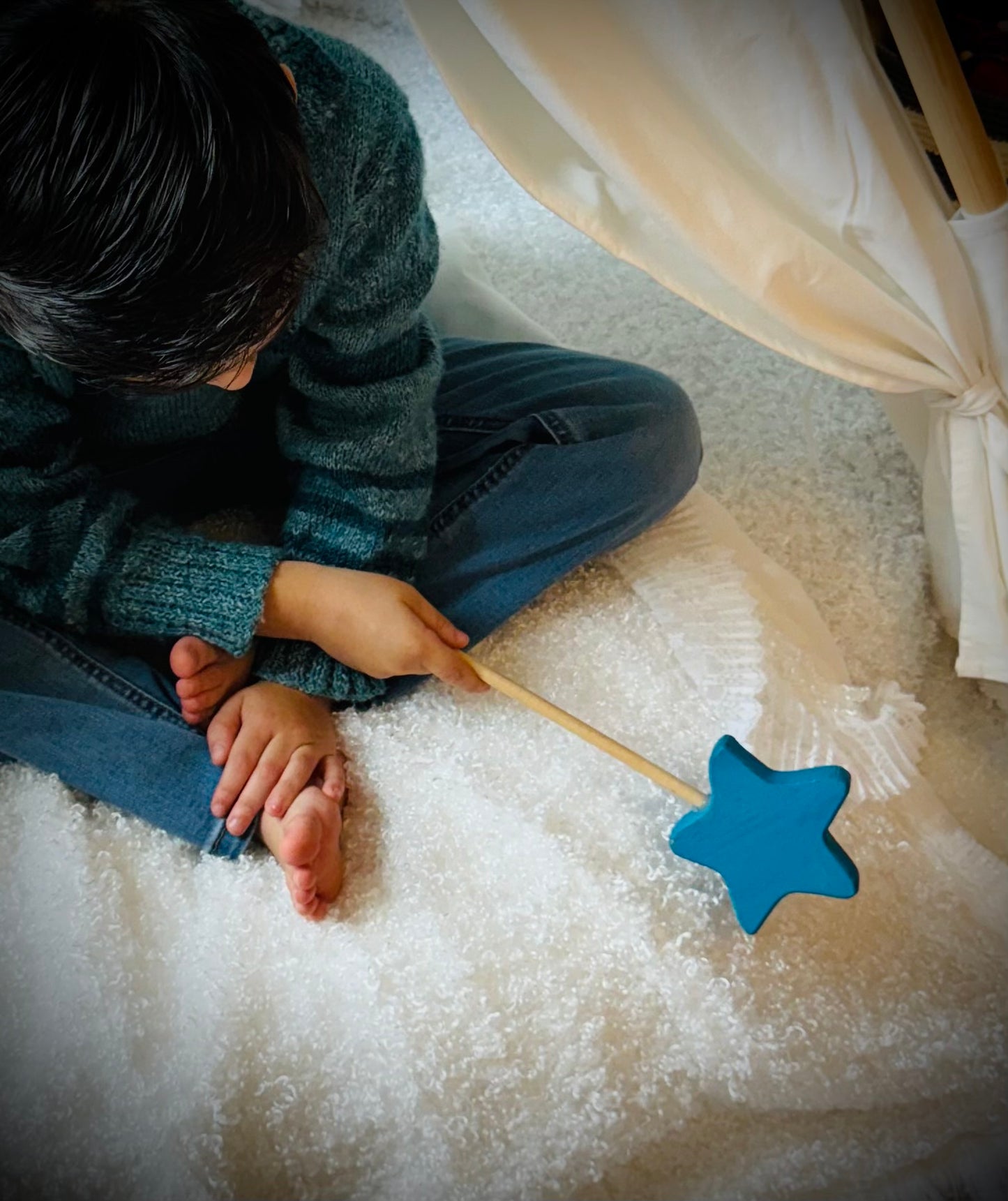 Child playing with a colorful wooden magic wand toy with a blue star tip indoors