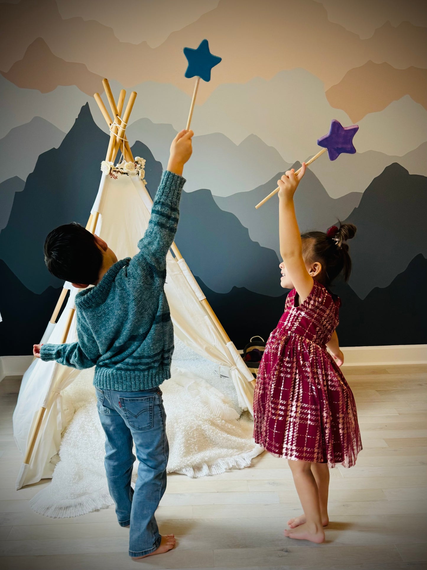 Two children playing indoors with colorful wooden magic wand toy near a teepee tent
