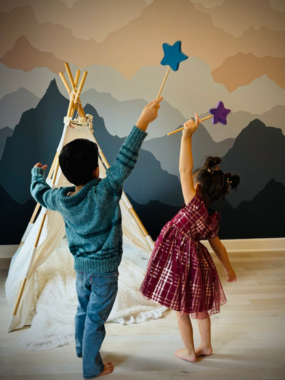Two kids playing indoors with colorful wooden magic wand toy in front of a teepee and mountain wall mural