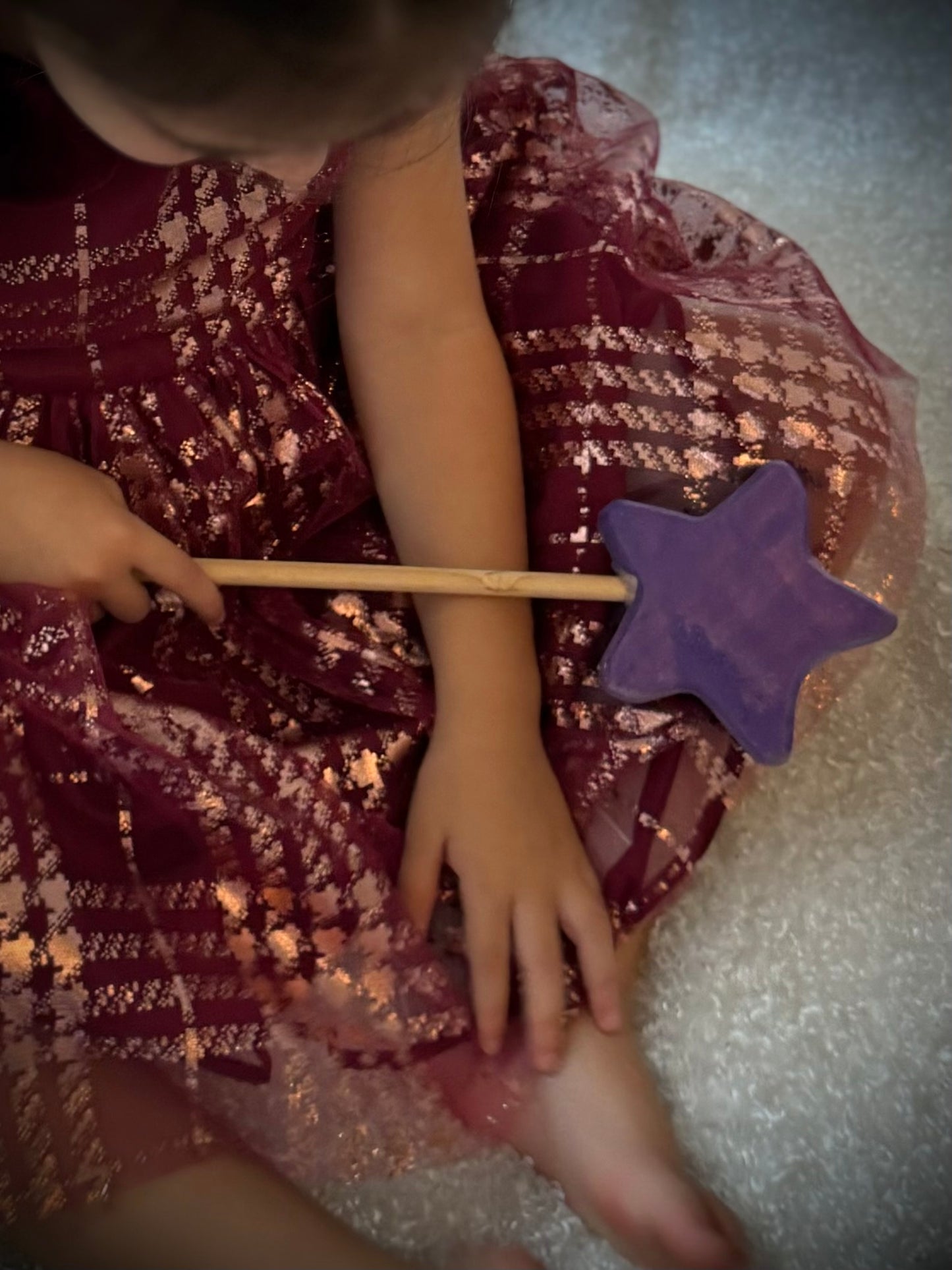 Child holding a colorful wooden magic wand toy with a purple star while wearing a sparkly dress