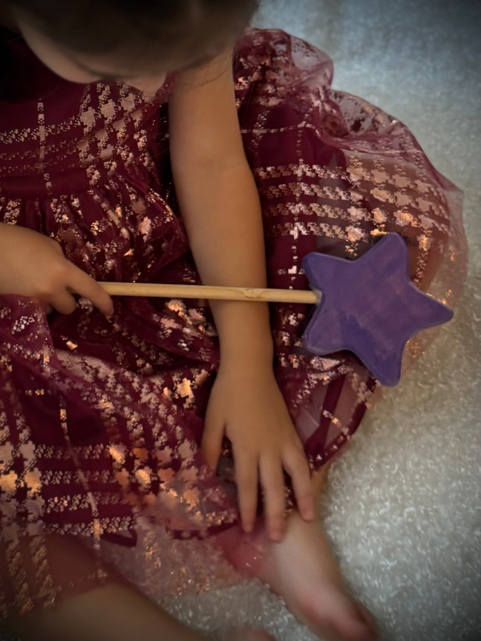 Child holding a colorful wooden magic wand toy with a purple star while wearing a sparkly dress