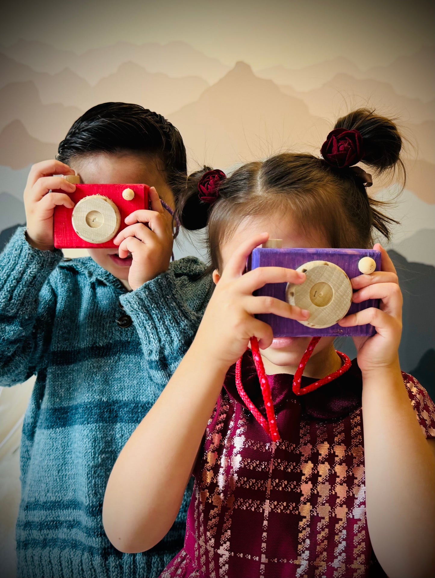 Two children playing with colorful handmade kids wooden camera toys indoors