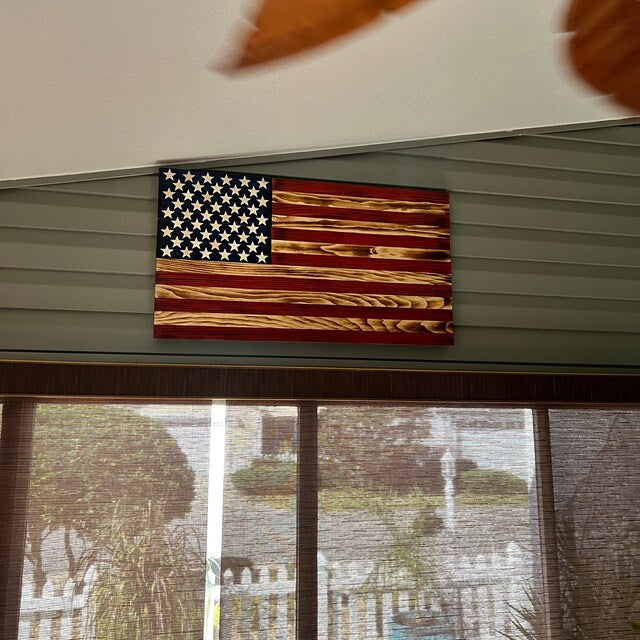 Wooden American Flag wall decoration mounted above windows in a room with gray siding wall