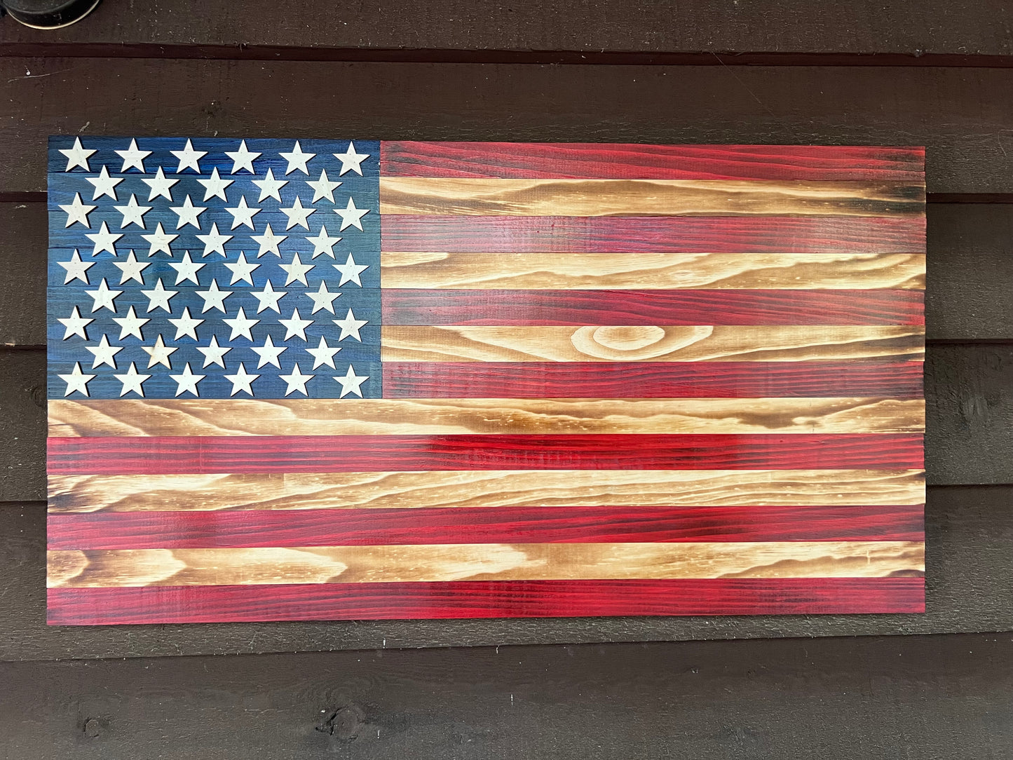Wooden American Flag with distressed red, white, and blue paint on natural wood grain background