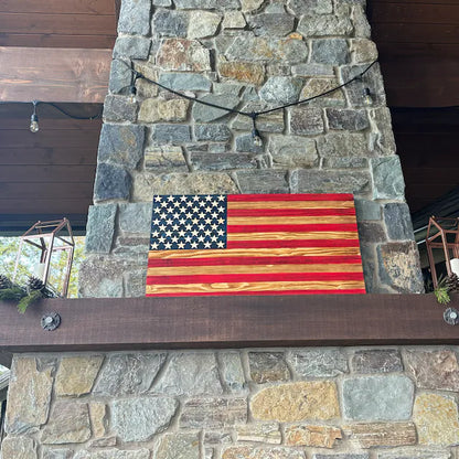 Wooden American Flag displayed on stone fireplace mantel in rustic indoor setting