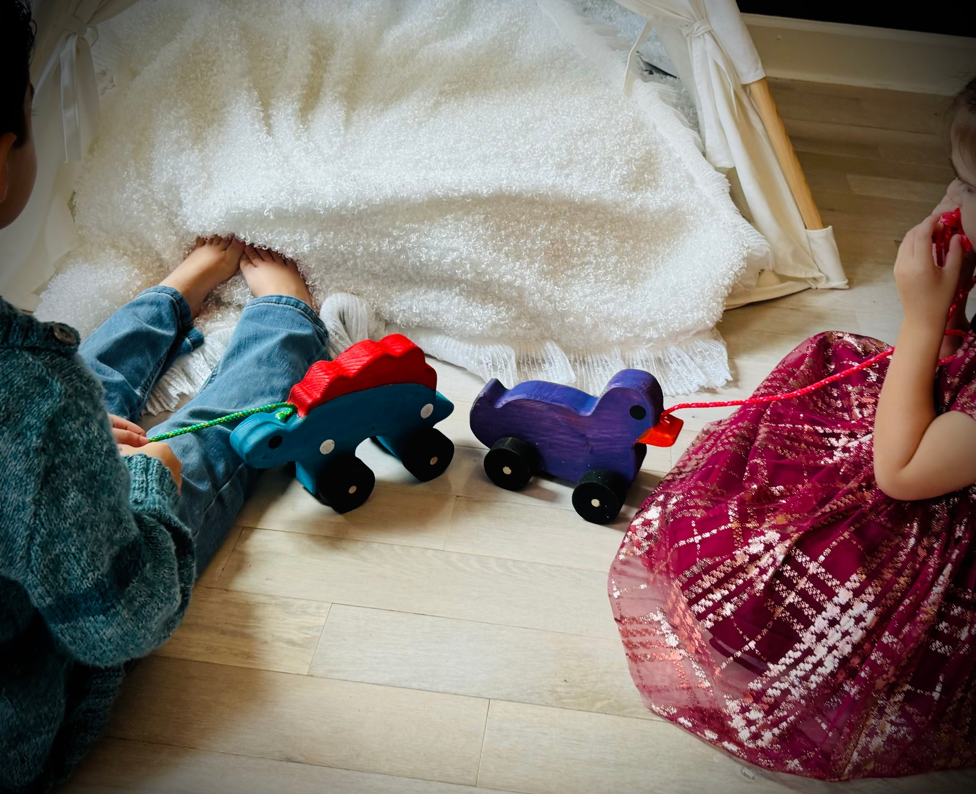 Children playing with colorful wooden pull duck toys on wooden floor near a cozy tent