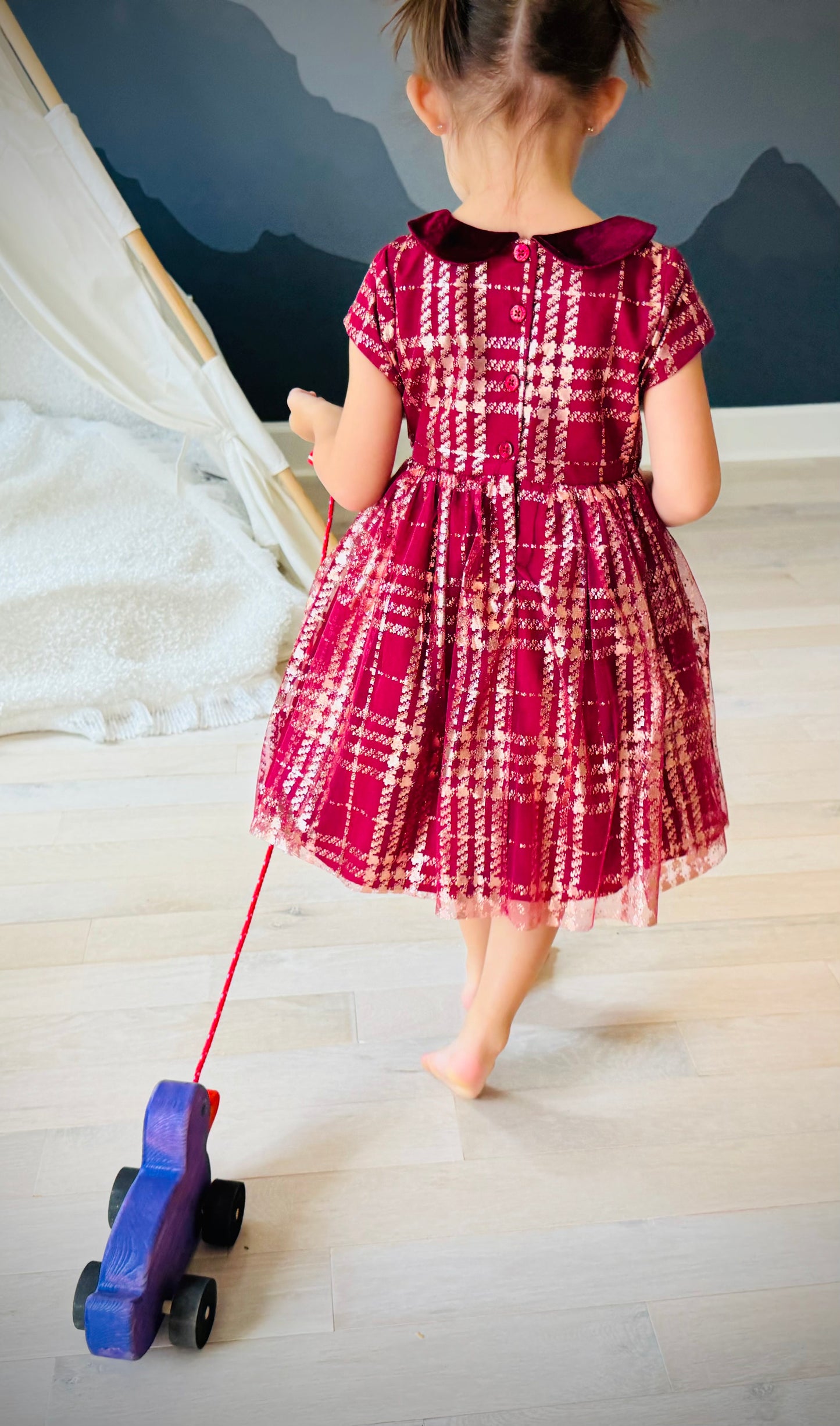 Child pulling a purple wooden pull duck toy on wheels with a red string on a light wood floor