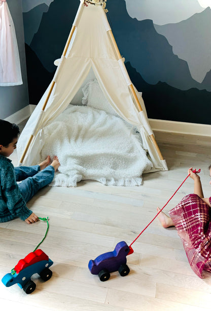 Children playing with wooden pull duck toys near a white play tent on a wooden floor