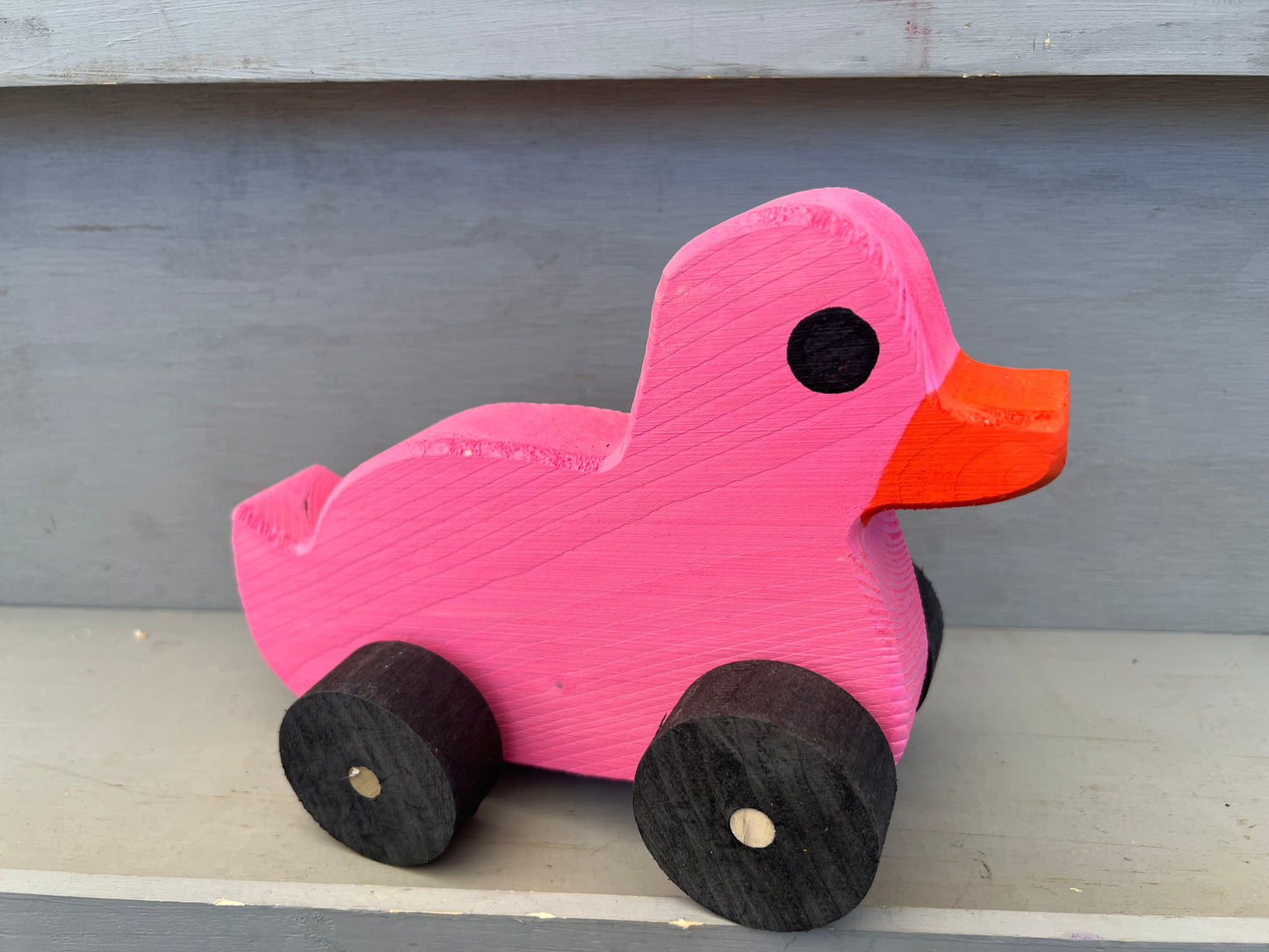 Bright pink wooden pull duck toy with black wheels and orange beak for children