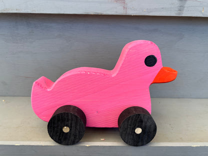 Pink wooden pull duck toy with black wheels and orange beak on gray surface