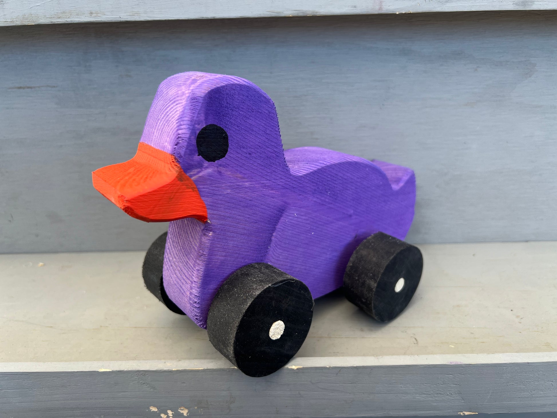 Purple wooden pull duck toy with orange beak and black wheels for children