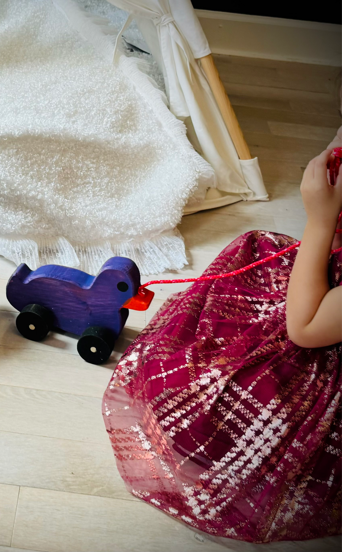 Child playing with a purple wooden pull duck toy on wheels on a light wooden floor