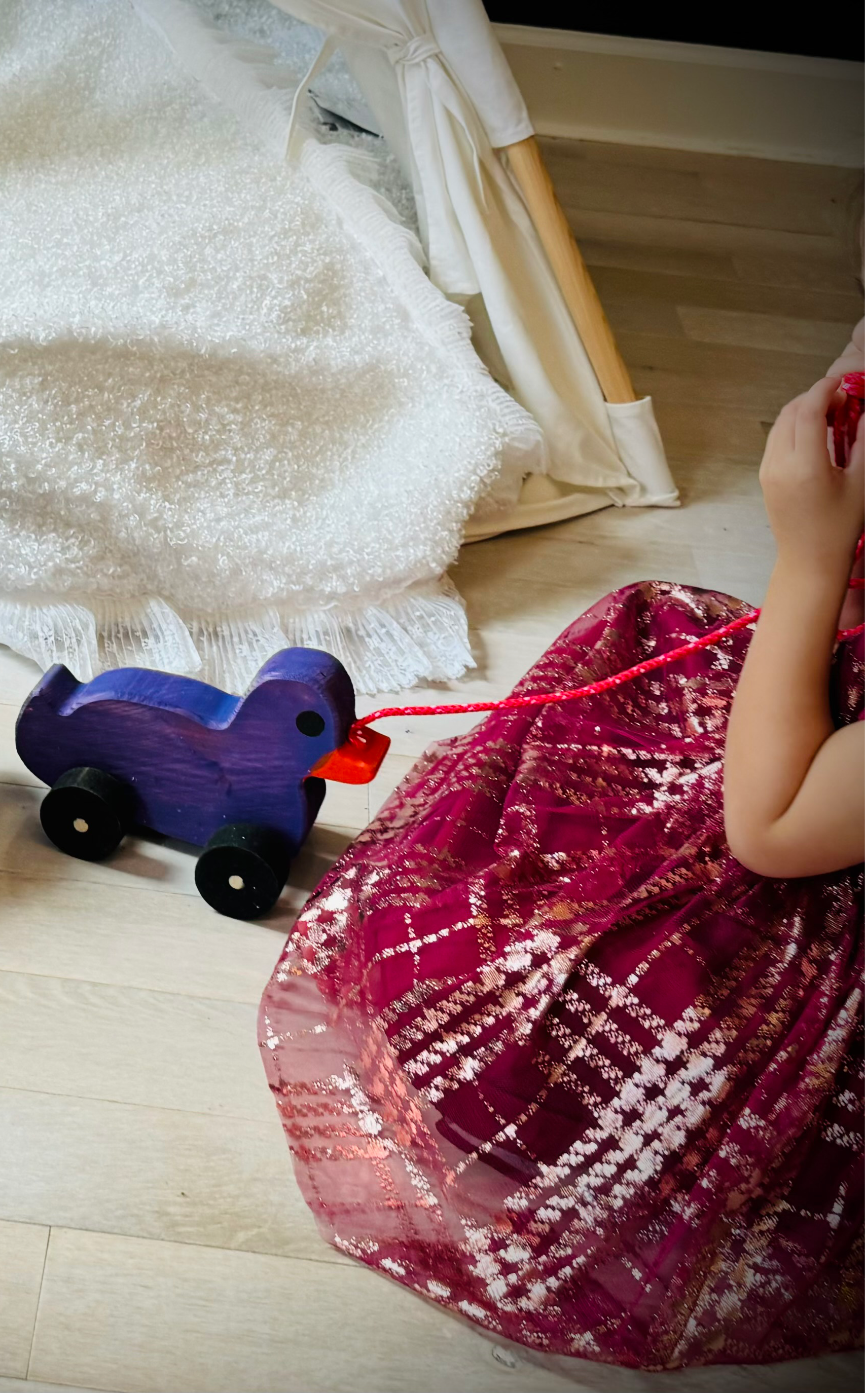 Child playing with a purple wooden pull duck toy on wheels on a light wooden floor