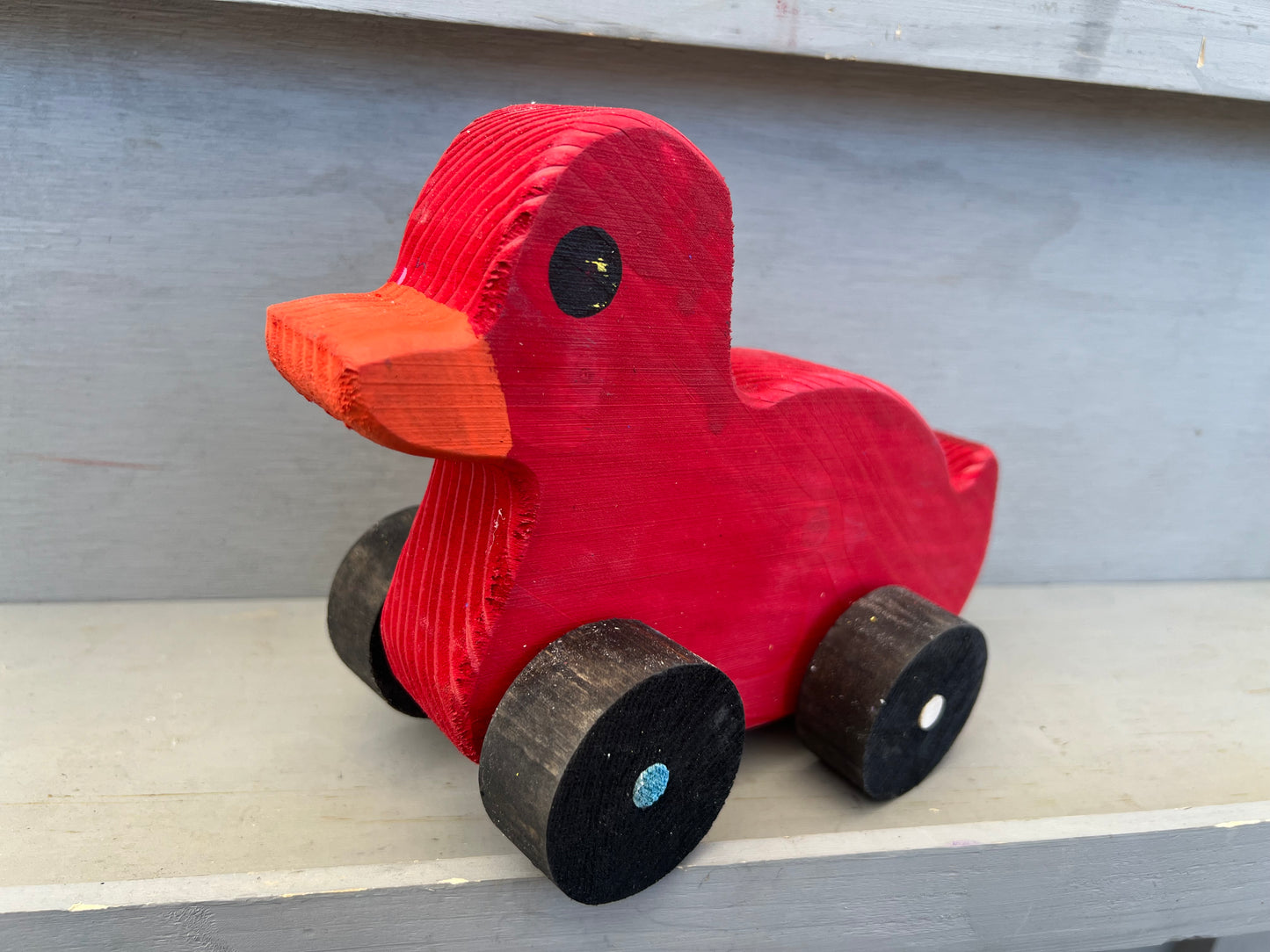 Red wooden pull duck toy with black wheels and orange beak for children’s playtime